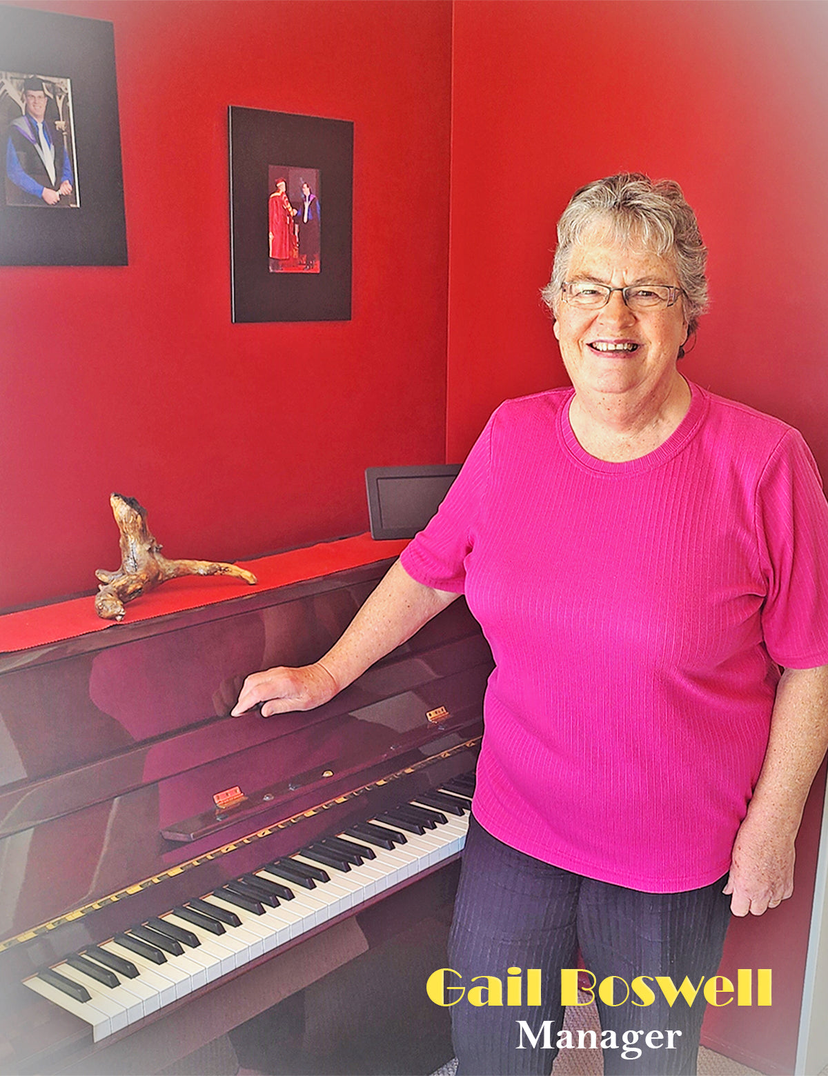 picture of miss gail boswell the school owner using a pink shirts in front a piano